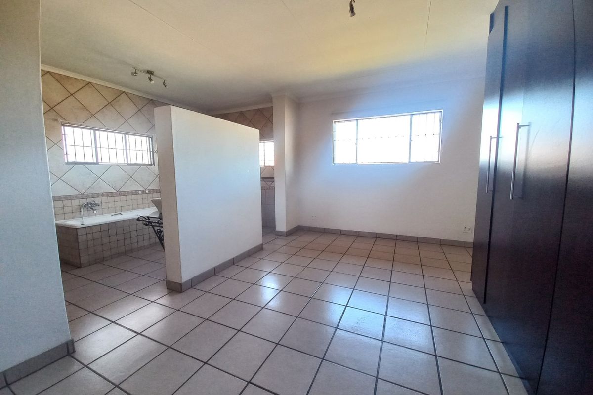 Spacious bedroom featuring tiled flooring, built-in cupboards, and an open-plan en-suite bathroom area with a built-in bathtub.