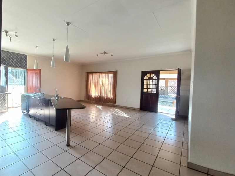 Spacious open-plan living and kitchen area featuring a central island, tiled flooring, and direct access to the exterior through timber doors.
