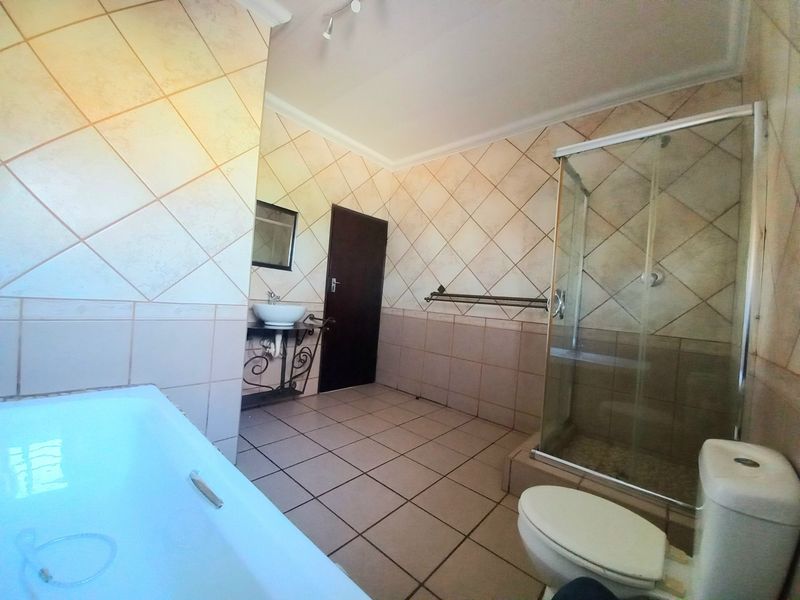 A spacious bathroom featuring a bathtub, a separate glass-enclosed shower, a toilet, and a vessel sink with tiled finishes throughout.