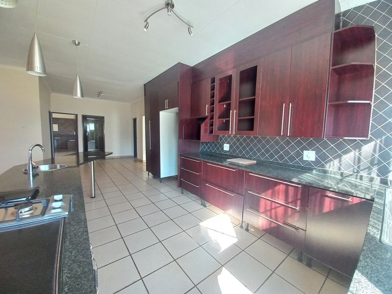 Spacious kitchen featuring dark wood cabinetry, granite countertops, a gas hob, and tiled flooring, offering a functional layout with ample storage space.