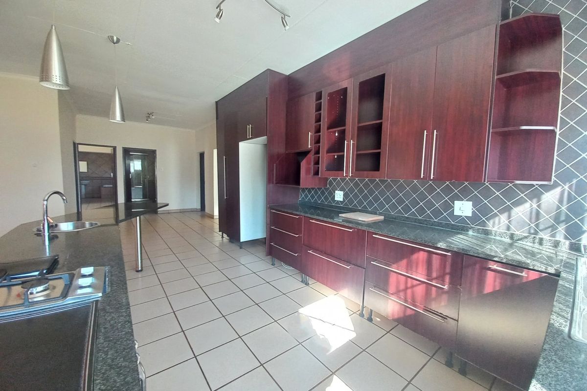 Spacious kitchen featuring dark wood cabinetry, granite countertops, a gas hob, and tiled flooring, offering a functional layout with ample storage space.