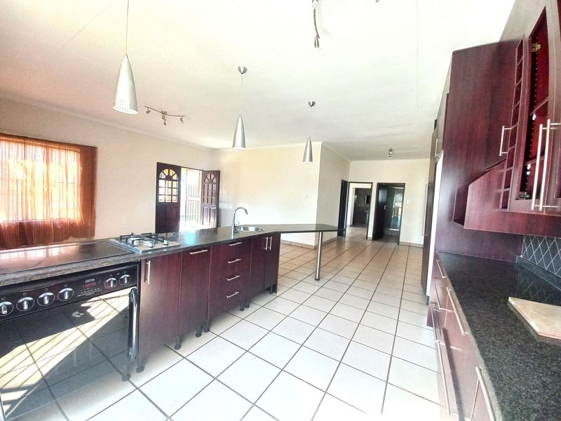 Spacious kitchen featuring dark wood cabinetry, granite countertops, a gas hob, and tiled flooring, offering a functional layout with ample workspace.