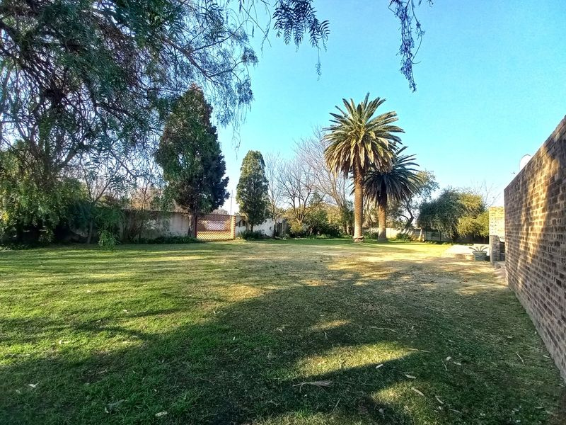 A spacious, well-maintained garden area featuring mature palm trees, expansive lawn, and a solid brick boundary wall.