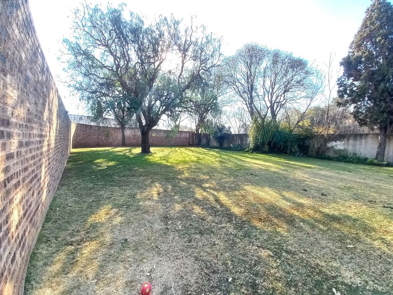 A spacious, private garden area featuring a large lawn, mature trees, and high brick boundary walls for added privacy.