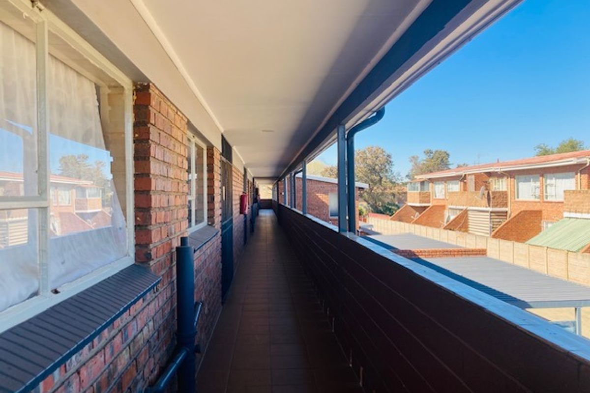 An exterior walkway or balcony featuring brick walls, tiled flooring, and metal railings, providing access to the residential units.