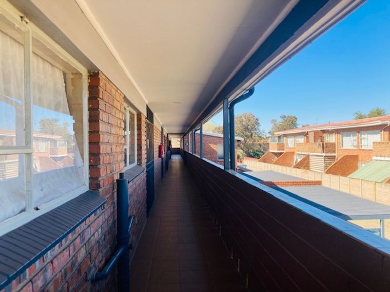 An exterior walkway or balcony featuring brick walls, tiled flooring, and metal railings, providing access to the residential units.