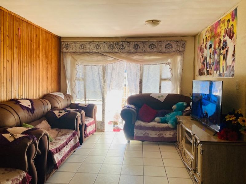 A living room featuring timber wall paneling, tiled flooring, and a sliding glass door providing access to the exterior.