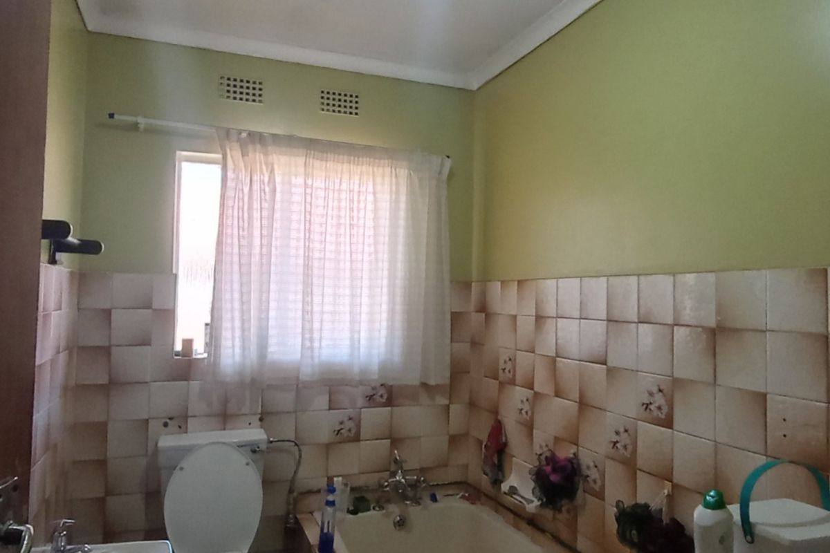 A dated bathroom featuring a bathtub, toilet, and basin with partially tiled walls requiring cosmetic updates.