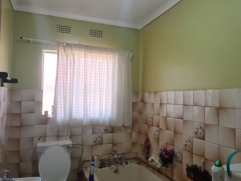 A dated bathroom featuring a bathtub, toilet, and basin with partially tiled walls requiring cosmetic updates.