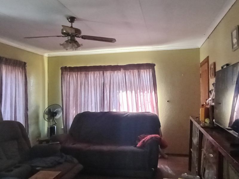 A living room featuring a ceiling fan and coved cornicing, requiring cosmetic updates to improve the overall aesthetic and appeal.