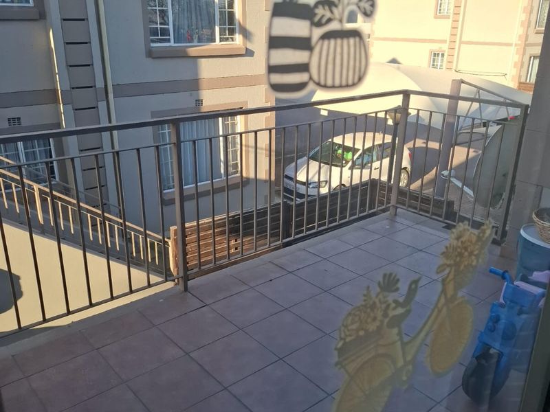 A tiled balcony featuring a metal balustrade, overlooking the apartment complex parking area.