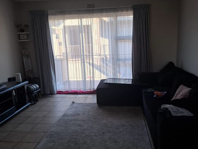 A living room featuring tiled flooring and a large sliding glass door that provides access to an outdoor balcony area.