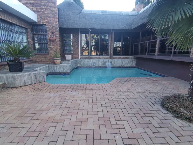 Outdoor pool area featuring brick paving, stone-clad water feature, and a thatched roof structure, providing a private entertainment space.