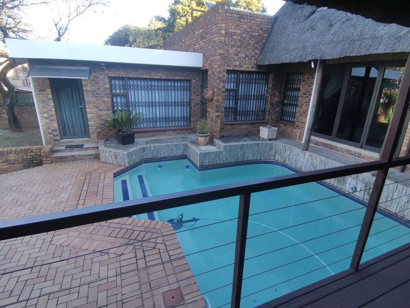 Outdoor pool area featuring a swimming pool, brick paving, and a face brick facade with a thatched roof section.