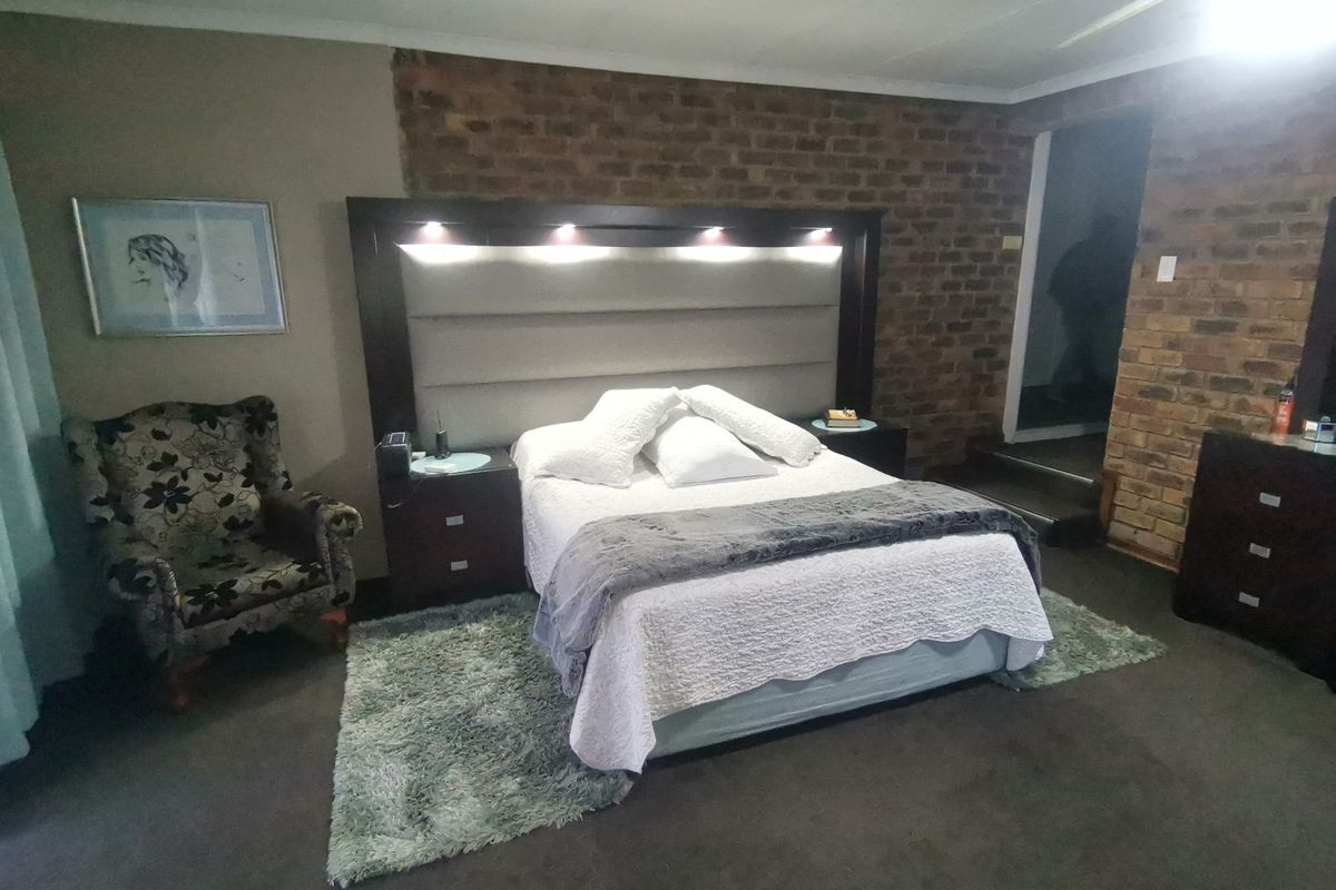 Spacious bedroom featuring an exposed brick feature wall and a built-in headboard with integrated accent lighting.
