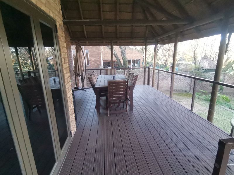 A spacious covered patio featuring timber decking, a traditional thatched roof, and glass sliding doors, overlooking the rear garden area.