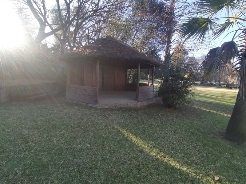 A garden setting featuring a traditional thatched gazebo with a brick base, situated in a spacious lawn area.