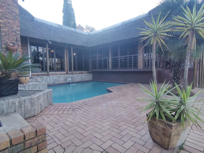 Outdoor pool area featuring a swimming pool, brick paved patio, and a thatched roof structure with a raised stone planter.