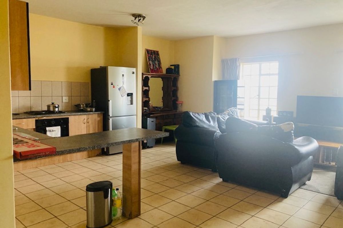 Open-plan living area featuring a kitchen with built-in cabinetry, oven, hob, and tiled flooring, seamlessly flowing into the adjacent living space.