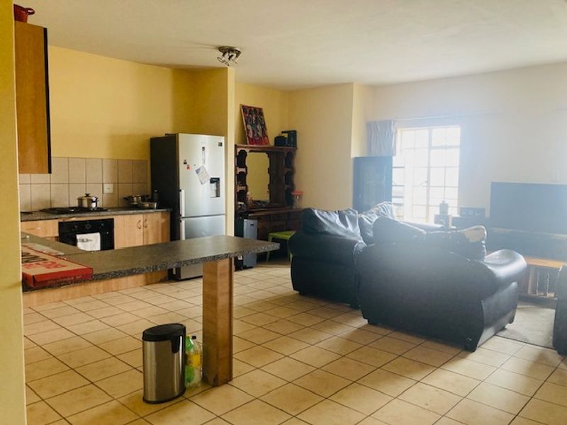 Open-plan living area featuring a kitchen with built-in cabinetry, oven, hob, and tiled flooring, seamlessly flowing into the adjacent living space.