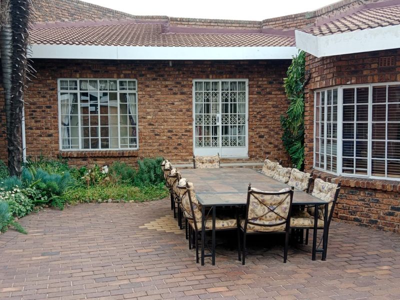 A paved outdoor patio area featuring exposed brick walls, grid-style windows, and security doors, providing a functional space for outdoor dining.