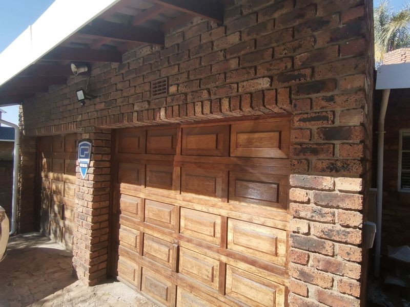 Exterior view of a double garage featuring exposed brick construction and traditional timber sectional doors with overhead timber rafters.