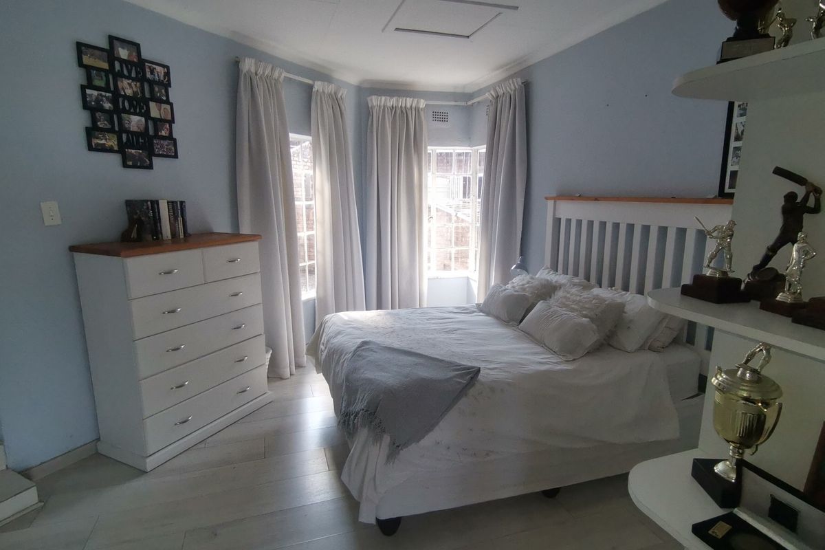 A well-lit bedroom featuring a bay window, light-toned tiled flooring, and a neutral color palette, providing a comfortable and functional living space.