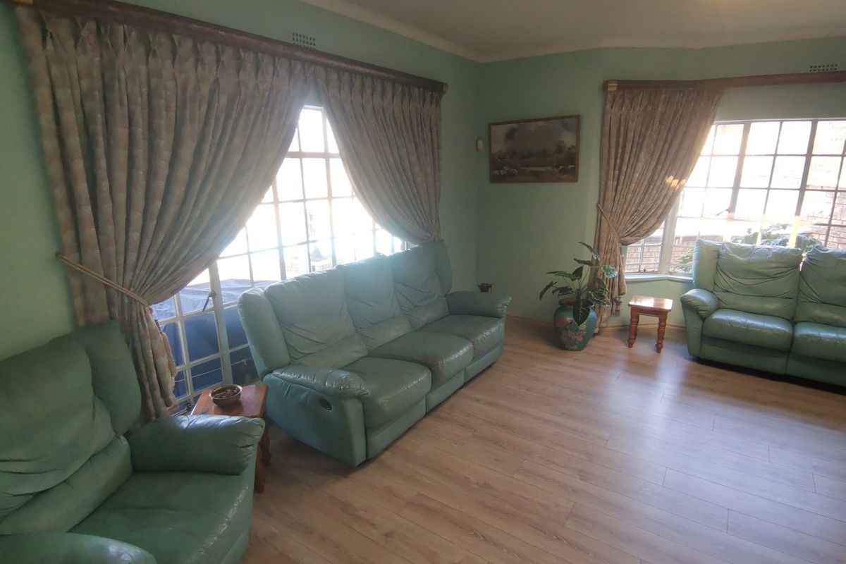 A spacious living room featuring light-toned laminate flooring, large bay windows, and classic coving, offering a bright and functional living space.