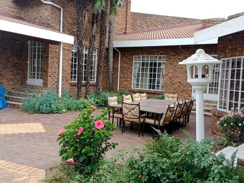 A spacious paved outdoor patio area featuring a classic brick facade, tiled roofing, and established garden surroundings, ideal for outdoor dining and entertaining.