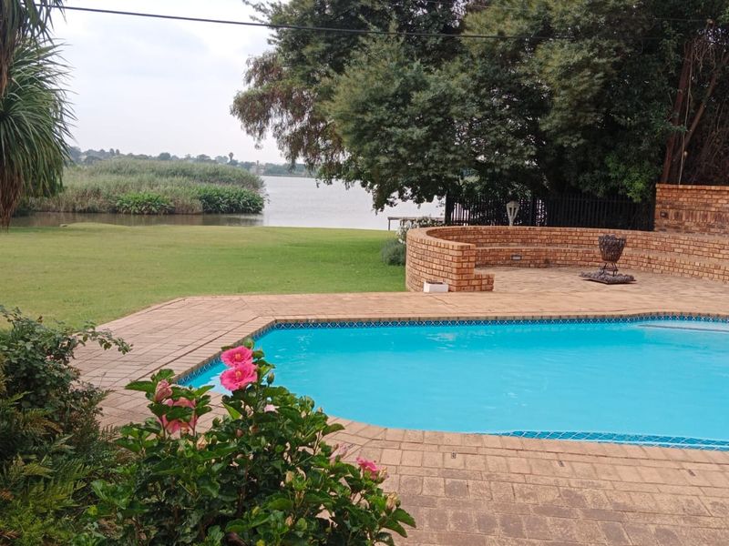 Outdoor pool area featuring a brick-paved patio, curved brick retaining wall, and direct views of the adjacent lake and garden.
