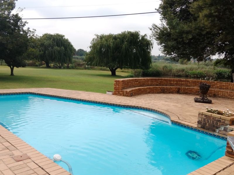 Outdoor pool area featuring a paved deck, curved brick retaining wall with built-in seating, and views over a spacious garden and natural landscape.
