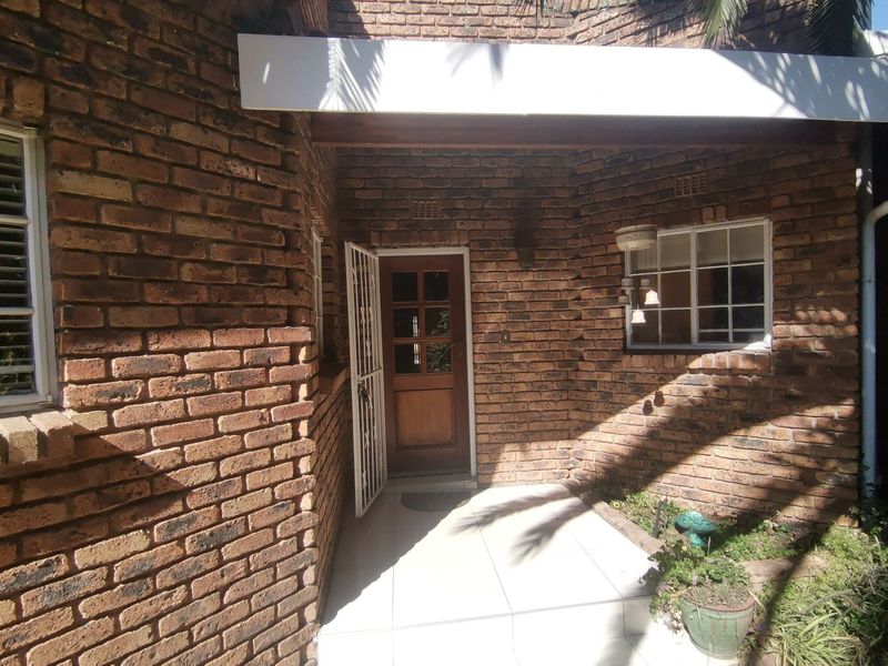 Front entrance area featuring exposed brickwork, a tiled porch, and a timber-framed door with a security gate.