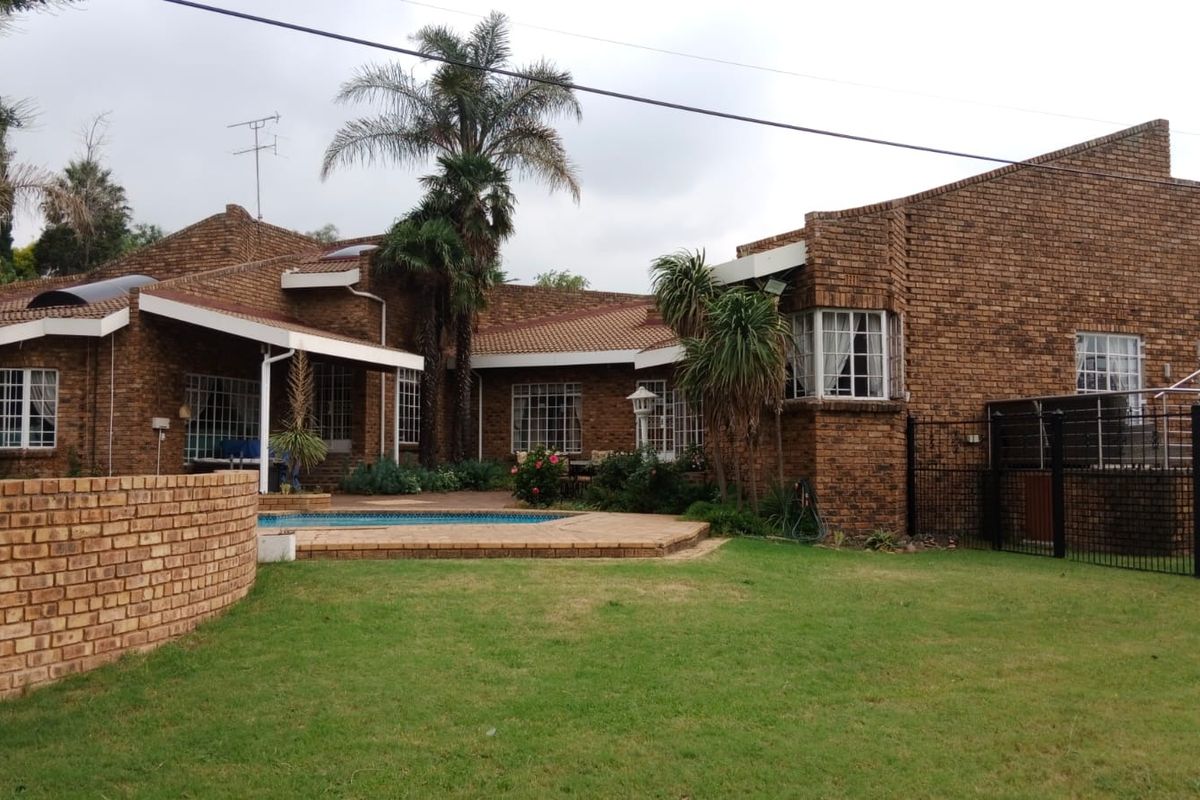 Rear view of a face brick house featuring a swimming pool, paved pool deck, covered patio area, and established garden.