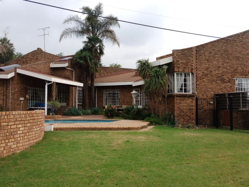 Rear view of a face brick house featuring a swimming pool, paved pool deck, covered patio area, and established garden.