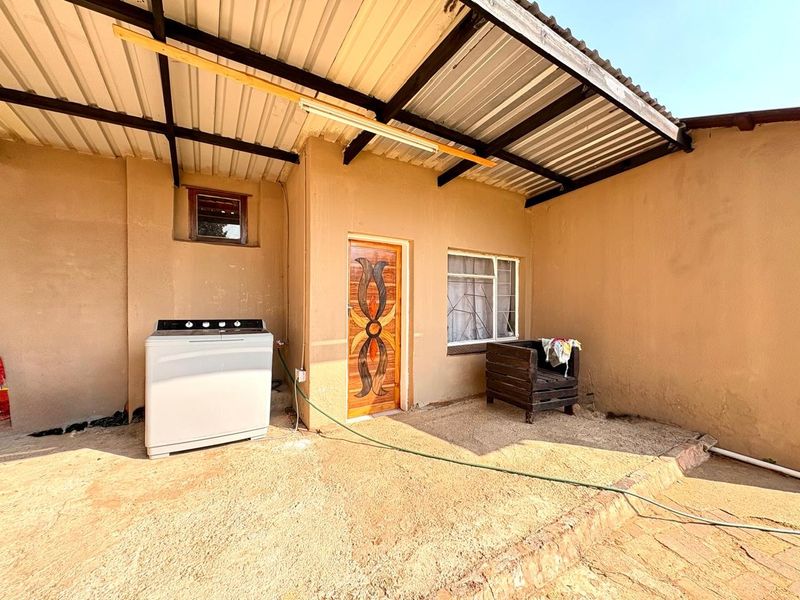 A covered outdoor patio area featuring a corrugated metal roof, concrete flooring, and a decorative timber door with security bars.