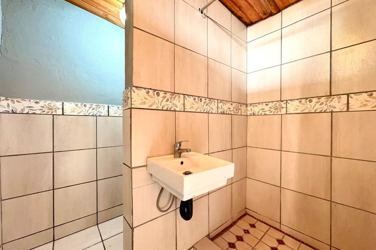 A compact bathroom featuring a wall-mounted basin, tiled walls with decorative border, and a timber ceiling, requiring modernization of fixtures and finishes.