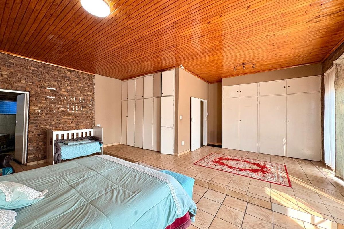 Spacious bedroom featuring a timber ceiling, exposed brick wall, and extensive built-in cupboard storage with tiled flooring throughout.