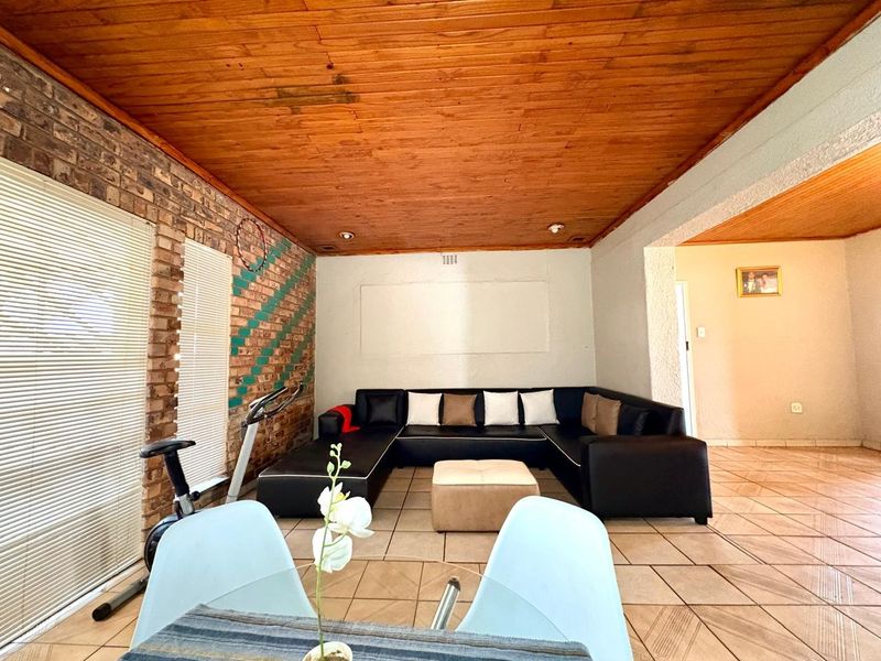 Spacious living area featuring a distinctive exposed brick wall, ceramic tiled flooring, and a warm timber tongue and groove ceiling.