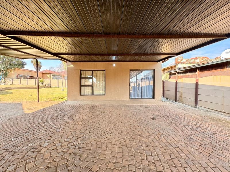 A covered outdoor patio area featuring a paved floor and corrugated metal roofing, providing a functional space for outdoor living.