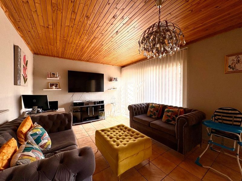 A living room featuring a warm timber tongue and groove ceiling, ceramic tiled flooring, and a decorative chandelier.