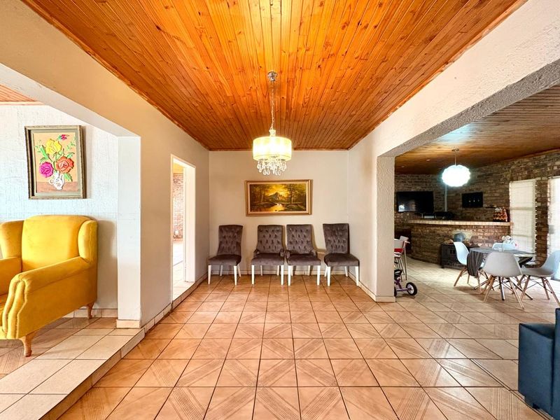 Spacious open-plan living area featuring a warm timber ceiling, ceramic tiled flooring, and an adjoining brick-accented bar space.