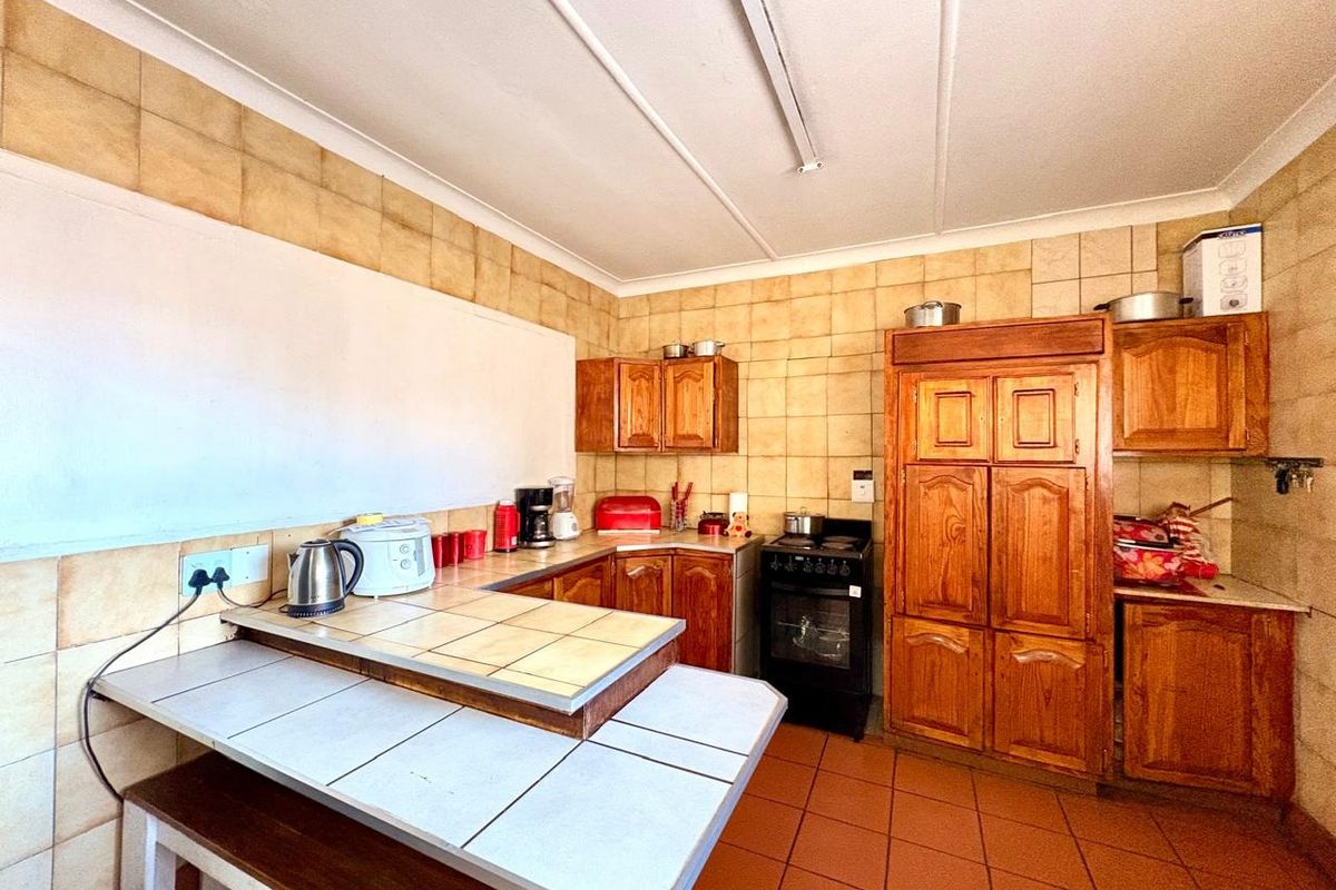 A dated kitchen featuring traditional wooden cabinetry, tiled countertops, a tiled backsplash, and a freestanding oven, offering potential for a modern renovation.