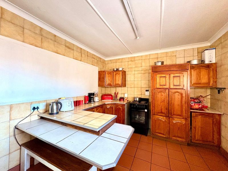 A dated kitchen featuring traditional wooden cabinetry, tiled countertops, a tiled backsplash, and a freestanding oven, offering potential for a modern renovation.