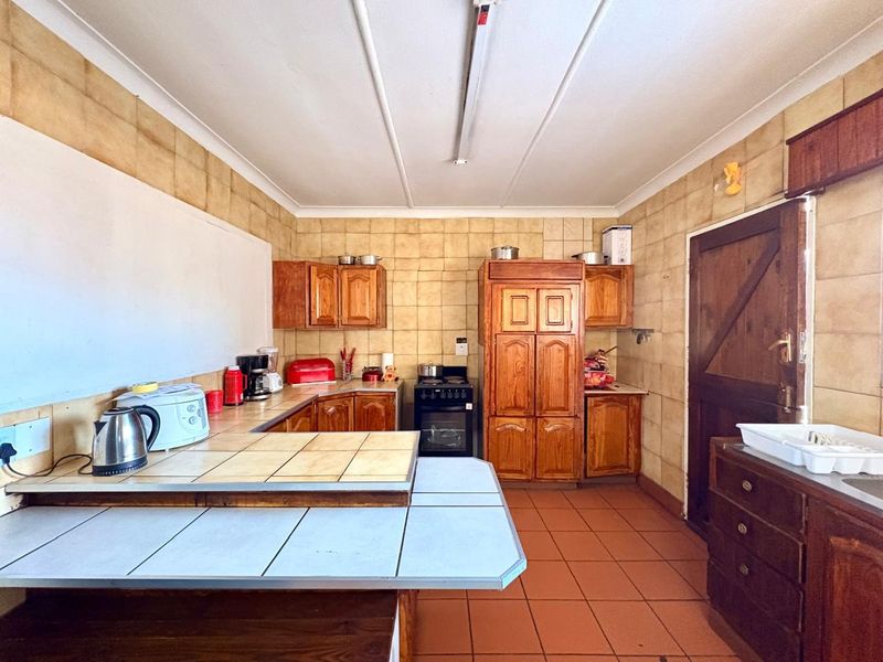 A dated kitchen featuring wooden cabinetry, tiled countertops, and tiled wall finishes, offering a functional layout with potential for modern renovation.
