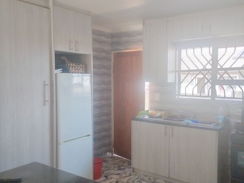 A functional kitchen featuring light-toned built-in cabinetry, patterned tiled flooring, and a window with security bars, providing a practical workspace.