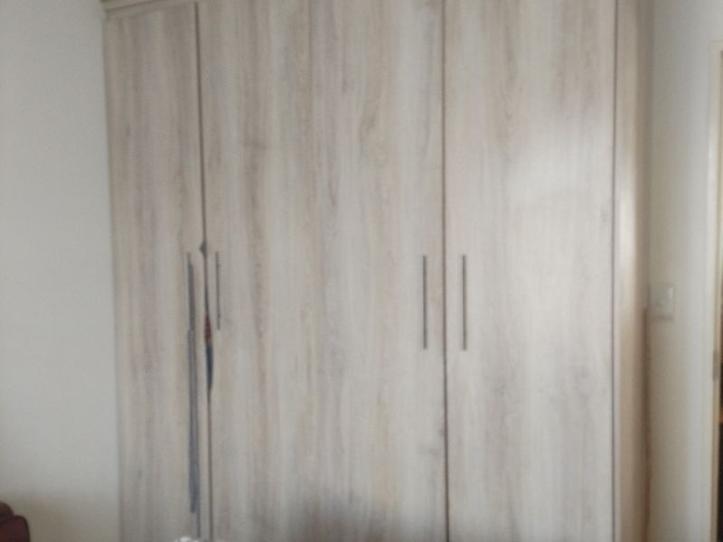 A bedroom featuring a large, modern light wood-grain built-in wardrobe with vertical handles.
