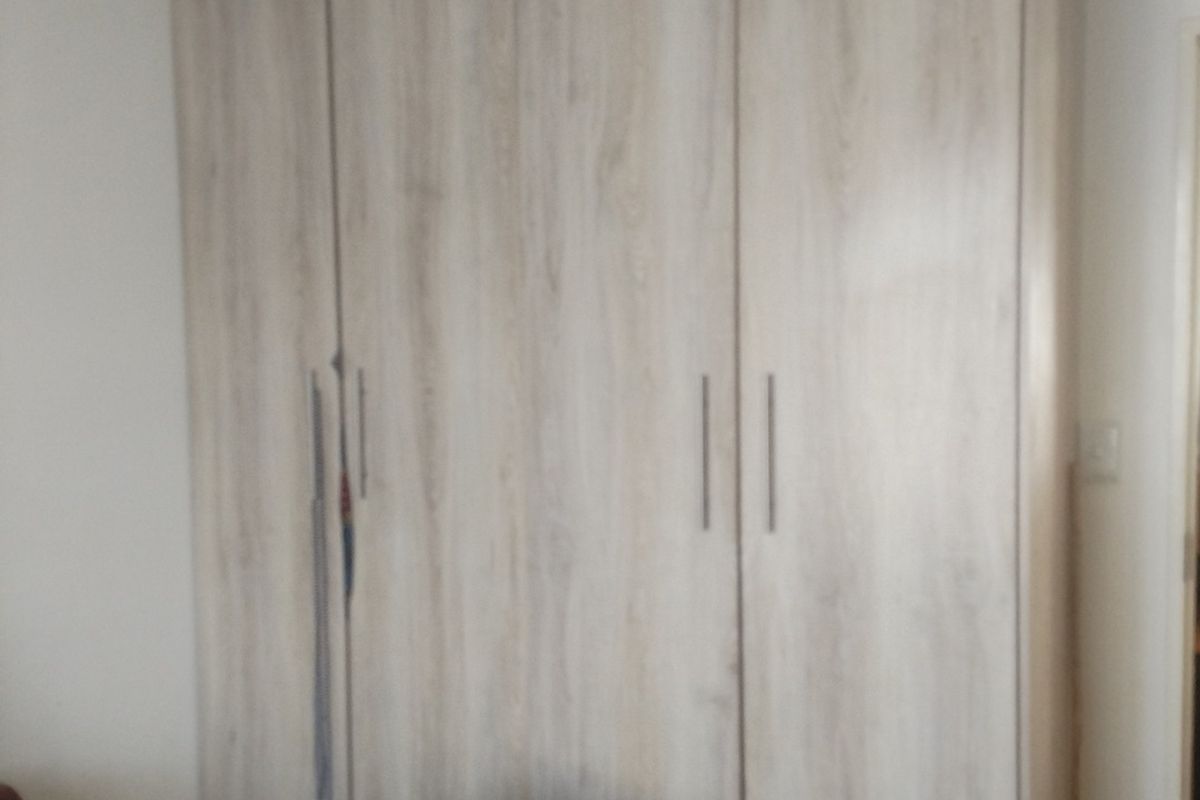 A bedroom featuring a large, modern light wood-grain built-in wardrobe with vertical handles.
