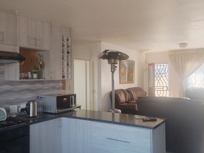 Open-plan kitchen and living area featuring modern light-wood cabinetry, dark stone countertops, and integrated appliances, flowing into a comfortable lounge space.
