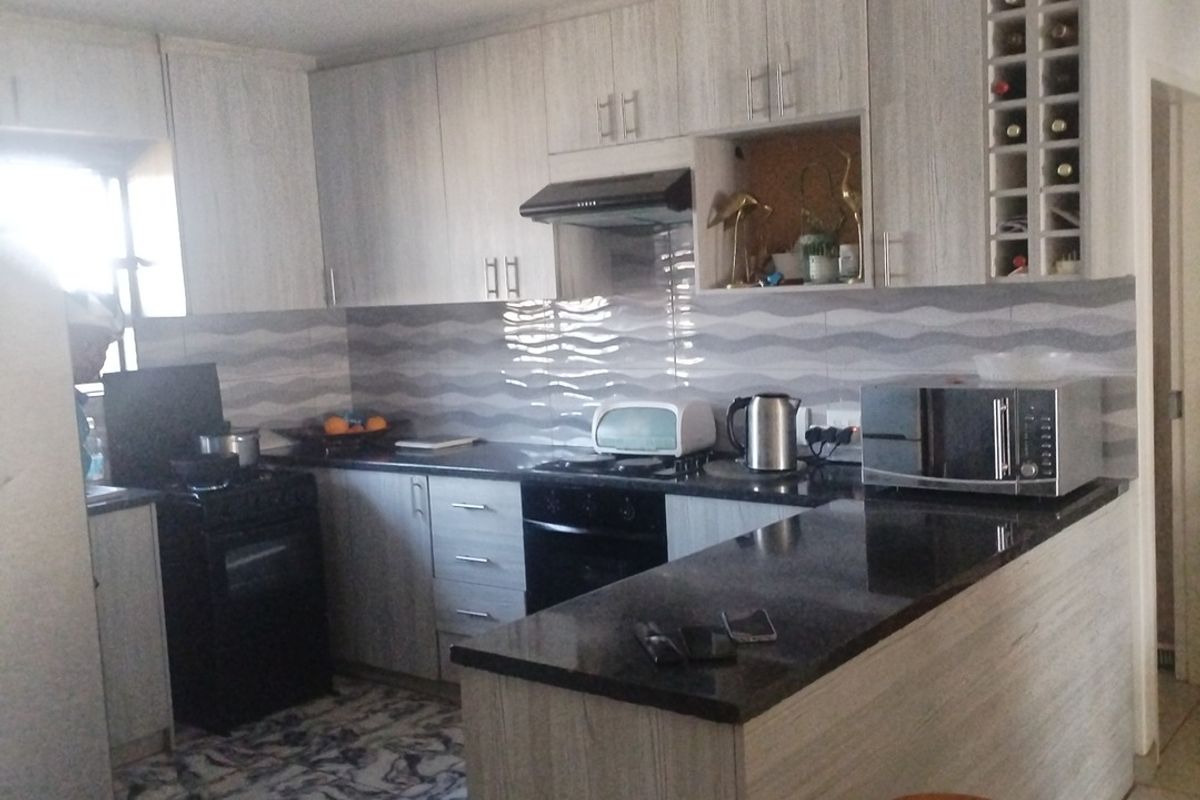 A functional kitchen featuring light wood-grain cabinetry, dark granite countertops, a breakfast bar, and a tiled backsplash with integrated oven and extractor fan.