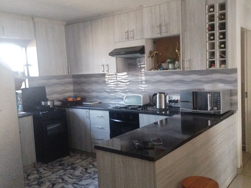 A functional kitchen featuring light wood-grain cabinetry, dark granite countertops, a breakfast bar, and a tiled backsplash with integrated oven and extractor fan.